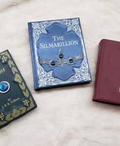Three leather bound Tolkien books -- A deep green leather bound The Hobbit with an Arkenstone in the middle; a blue and silver leather bound Silmarillion; and a red leather The Lord of the Rings Trilogy.