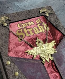 Unique 3D cover of D&D's Curse of Strahd. Brown leather folds over the velvet cover in the shape of a coffin with a large gold pendant chained to the front.