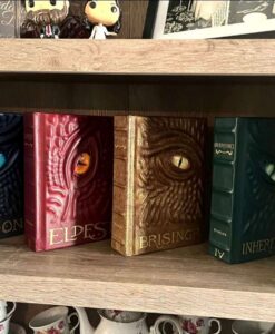 Four shiny leather Inheritance Cycle dragon books on a shelf; one blue, one red, one gold, and one dark green. All with a single bright eye in the center.