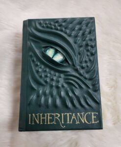 A forest green leather bound Inheritance by Christopher Paolini. The cover is ridged with the face of a dragon and a piercing light green eye.