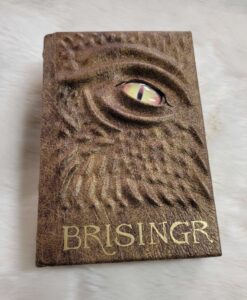 A buff brown leather bound Brisingr, by Christopher Paolini. The cover is raised with a ridged dragon face and a luminous yellow eye.
