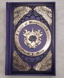 A Court of Wings and Ruin lovingly wrapped in purple leather and decorated with intricate golden wings wood filigree.